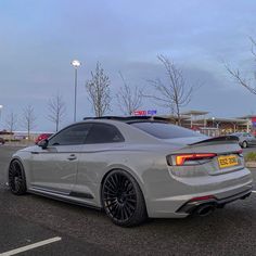 the rear end of a silver car parked in a parking lot next to a gas station