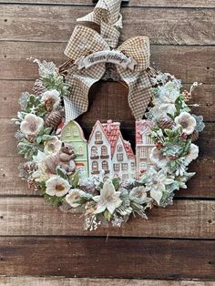 a wreath that has some houses and flowers in it on a wooden surface with a bow