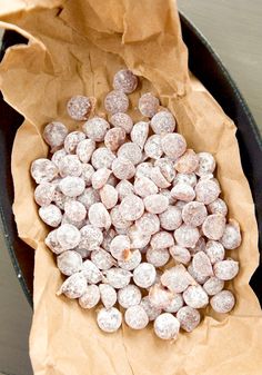 a pan filled with powdered donuts sitting on top of a wooden table next to a paper bag