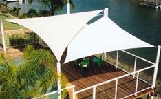 a white awning on top of a wooden deck next to water