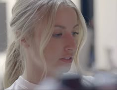 a woman with blonde hair is looking at her cell phone while she's wearing a white shirt