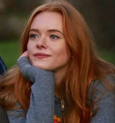 a woman with red hair and blue eyes is sitting next to a man who has his hand on her chin