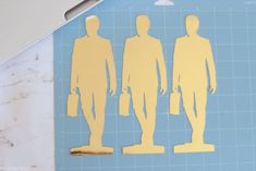 cut out paper figures of three men on a cutting board with scissors and ruler next to them