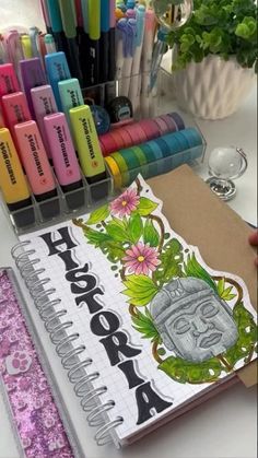 an open notebook with markers and pens in front of it on a table next to a potted plant