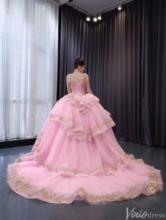 a woman in a pink ball gown looking down at the floor with curtains behind her