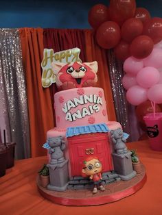 a pink and red birthday cake sitting on top of a table next to some balloons