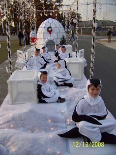 several children dressed in costumes sitting on ice blocks with lights strung from the sides and around them