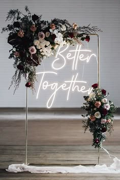 a neon sign that says better together with flowers and greenery on it in front of a white backdrop