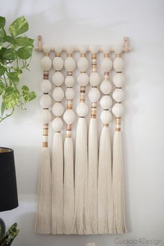 a white wall hanging with tassels on it next to a potted plant