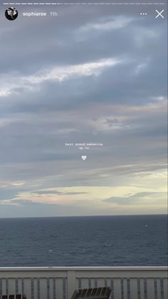 two wooden chairs sitting on top of a balcony next to the ocean under a cloudy sky