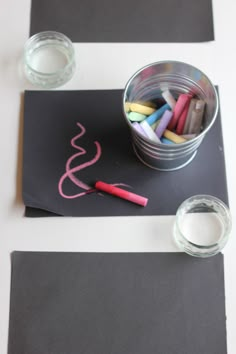 some crayons are sitting in a bucket on top of a black paper with pink writing