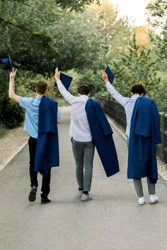 three people walking down a path with graduation caps in their hands