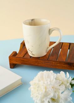 a white coffee cup sitting on top of a wooden tray next to a flower vase