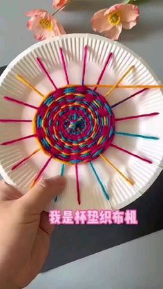 a person holding up a paper plate with yarn on it