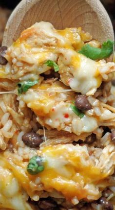 a wooden spoon filled with rice and beans covered in cheese, meat and green onions