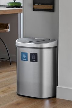 a stainless steel trash can sitting on top of a hard wood floor next to a wall