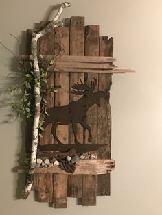 a wooden wall hanging with a moose cut out on it's side next to a tree branch