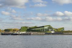 a large body of water next to a building with green roof and grass on top