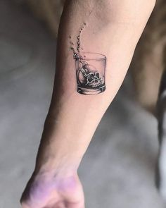 a person with a tattoo on their arm is holding a glass filled with water and ice cubes