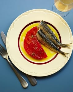 a fish on a plate next to a glass of water and fork, knife and spoon