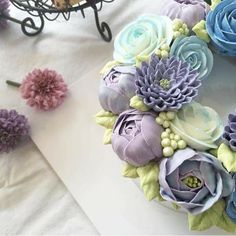 a wreath made out of fake flowers sitting on top of a white table next to purple and blue flowers