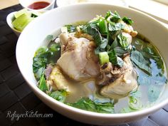 a white bowl filled with meat and greens on top of a black table next to a window