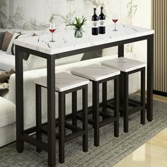 a table with three stools and two bottles of wine on it in front of a couch