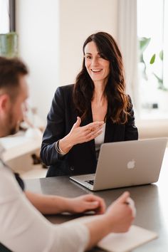 a woman sitting in front of a laptop computer talking to another person at a table