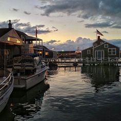 several boats are docked in the water near houses and buildings at dusk with clouds above them