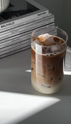 an iced drink with ice sits on a table next to stack of books and magazines