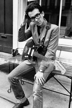 a man sitting on a bench with a guitar in his hand while talking on the phone