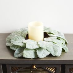 a white candle is sitting on top of a table with a green leafy wreath