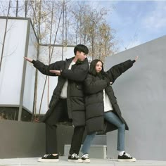 a man and woman standing next to each other on top of a cement wall with trees in the background