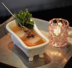 a small white bowl filled with food on top of a metal tray next to a candle