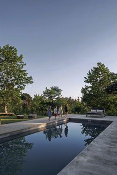 some people are walking near a pool in the middle of a yard with trees and bushes