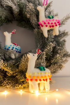 some llamas are hanging from a christmas wreath with lights on it and one is wearing a knitted sweater