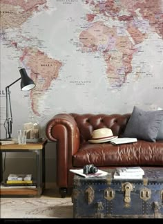 a brown leather couch sitting in front of a wall with a world map on it