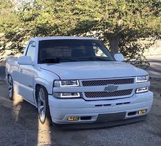 a white pickup truck parked in front of some trees and dirt area with no one around it