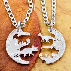 two silver necklaces with animals on them sitting on top of a fall leaf in the sun