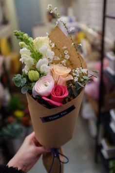 a person holding a brown paper bag with flowers in it and greenery on the side