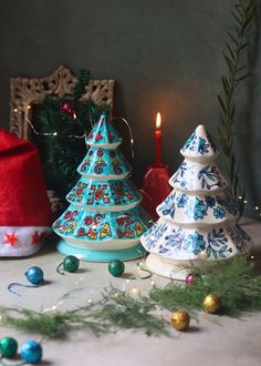 three ceramic christmas trees sitting on top of a table next to a lit candle and ornaments