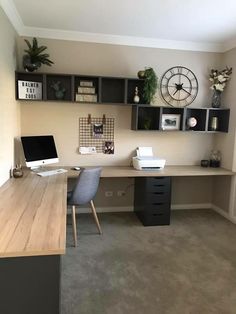 a desk with a computer on top of it next to a wall mounted clock and shelves