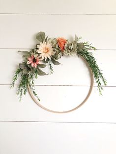 a circular wreath with flowers and greenery hanging on a white wooden wall in the shape of a circle