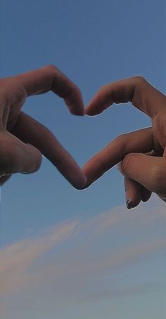 two hands making a heart shape with their fingers against a blue sky and white clouds