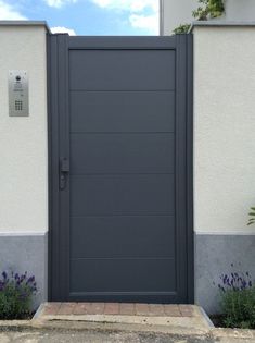 a large gray door in front of a white building with purple flowers on the side