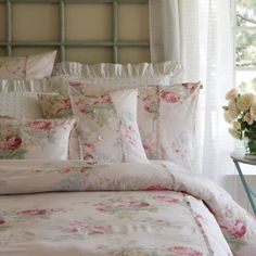 a bed with white and pink flowers on it in front of a window next to a table