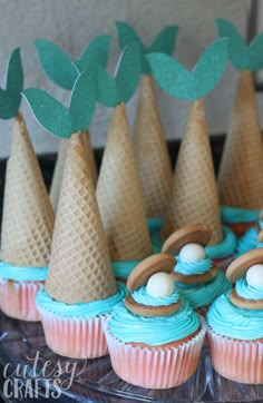 cupcakes with blue frosting and green leaves on top are arranged in cones