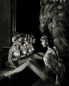 some very pretty ladies sitting in front of a mirror with feathers on their head and legs