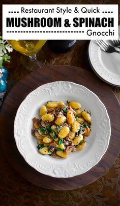 a white plate topped with pasta and mushrooms on top of a wooden table next to silverware