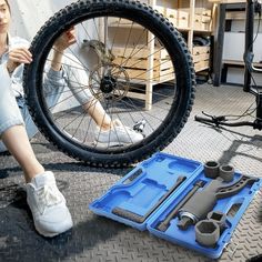 a woman sitting on the ground next to a bicycle tire and tools in a box